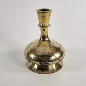 May include: A gold-colored metal vase with an ornate design. The vase has a round body and a narrow neck.