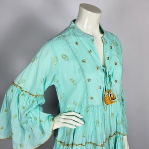 Indian fashion tunic in light turquoise/aqua, with golden embroidery. The deep V-neck can be closed by tying 2 strings, ending on a tassel with a natural Cowrie shell.