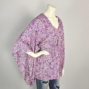 May include: A pink and purple patterned blouse with a V-neck and long, wide sleeves. The blouse has a cinched waist and a flowing, relaxed fit.