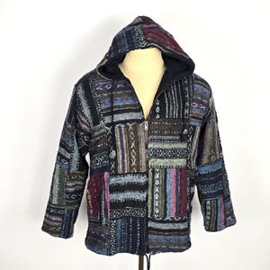 May include: A patchwork hooded jacket with a full zipper closure. The jacket features a variety of colorful fabric patches in shades of blue, purple, and brown. The hood is lined with black fabric, and the jacket has a drawstring at the bottom.