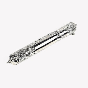 Puede incluir: Un estuche cilíndrico de plata con intrincados patrones florales y de volutas en relieve en ambos extremos, con una sección central lisa y pulida. El objeto de metal tiene un remate decorativo cónico en cada extremo y acabado metálico.