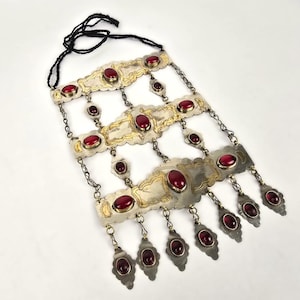 May include: A silver and gold necklace with red gemstone accents. The necklace has a chain link design and features multiple layers of decorative metalwork.