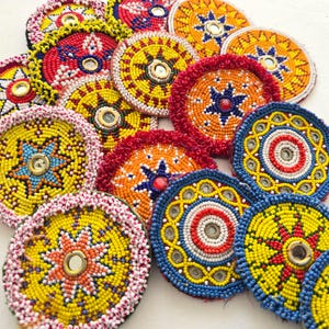 Könnte beinhalten: Eine Sammlung farbenfroher, mit Perlen besetzter Untersetzer in verschiedenen Designs. Die Untersetzer weisen komplizierte Muster mit roten, gelben, orangefarbenen und blauen Perlen auf, einige mit verspiegelten Zentren. Diese dekorativen Artikel sind ideal, um jedem Zuhause einen Hauch von Bohème zu verleihen.