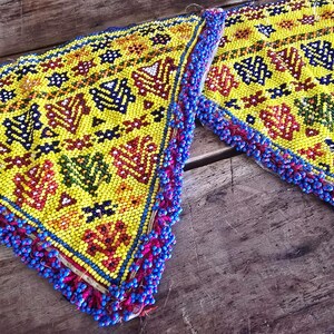 Puede incluir: Dos piezas triangulares de cuentas con fondo amarillo y patrones geométricos coloridos. Los bordes están recortados con cuentas azules y rosas.