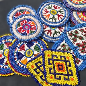 Puede incluir: Una colección de posavasos y piezas decorativas de cuentas coloridas. Los diseños presentan patrones intrincados en rojo, azul, amarillo y blanco, con formas circulares y cuadradas. Algunos tienen centros espejados.