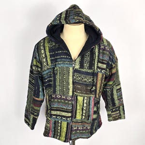 May include: A patchwork hoodie with a full zipper and a hood. The jacket features a variety of colors including green, blue, and brown. The design is made up of rectangular and square patches with geometric patterns.