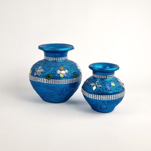 May include: Two blue ceramic vases with intricate designs and embellishments. The larger vase has a wider base and a more rounded shape, while the smaller vase is more slender. Both vases feature a silver trim and colorful floral accents.