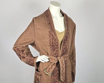 Puede incluir: Una larga gabardina de lana marrón con cuello chal y cinturón. La gabardina está bordada con un patrón floral burdeos.