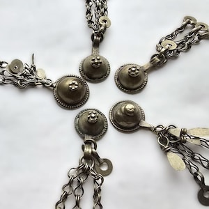 Può includere: Quattro ciondoli in metallo color argento con catene. Ogni ciondolo presenta una parte superiore rotonda e bombata con un motivo floreale decorativo. Le catene sono collegate tra loro in un motivo circolare.