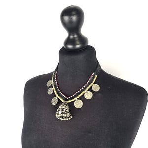 May include: A silver necklace with a bell pendant and coin charms. The necklace is made of black cord and has red and gold beads.