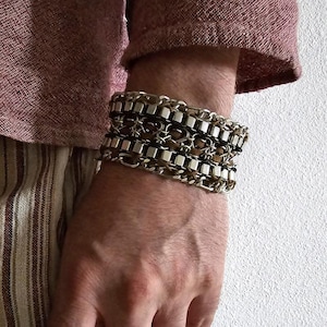 May include: A silver and black chain bracelet with multiple rows of links and square accents.