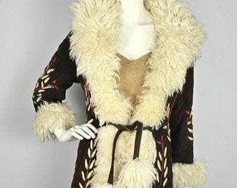 May include: A brown suede coat with a white faux fur collar and trim. The coat is embroidered with floral designs in red and white thread. The coat has a tie belt and pom-poms on the sleeves.