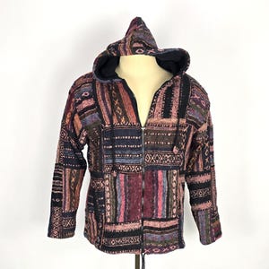 May include: A patchwork zip-up hoodie with a hood. The jacket features a variety of colors including burgundy, navy, and pink. The design includes geometric patterns and vertical stripes. The hoodie is displayed on a mannequin.