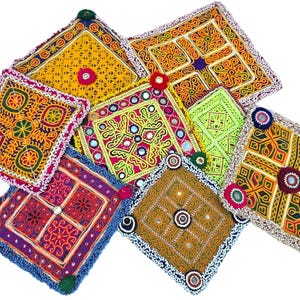 Op de afbeelding: Een verzameling kleurrijke, vierkante, geborduurde textielpatches. Elke patch heeft ingewikkelde patronen in verschillende kleuren, waaronder geel, rood, groen en blauw, met decoratieve spiegelaccenten en kralenranden. De patches zijn gerangschikt op een witte achtergrond.