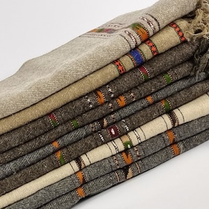 Puede incluir: Una pila de chales de lana tejidos en varios tonos de marrón, beige y gris con patrones geométricos coloridos. Los chales están doblados y superpuestos, creando una exhibición texturizada y visualmente atractiva.