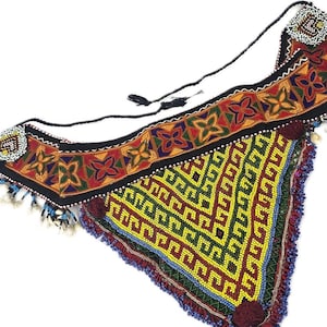 May include: A triangular textile accessory featuring a wide black band with embroidered orange, green, and blue floral motifs. The lower section is covered in yellow and green geometric beadwork, finished with blue beaded fringe and small white shells.