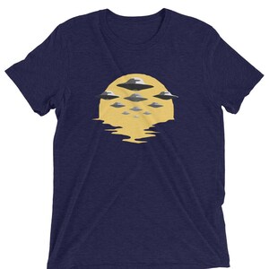 Puede incluir: Una camiseta azul marino con un gr&aacute;fico de un sol amarillo con varios OVNIs grises volando sobre &eacute;l.