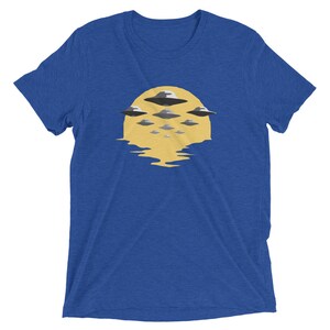 Puede incluir: Una camiseta azul real con un gr&aacute;fico de un sol amarillo con varios OVNIs grises volando sobre &eacute;l.