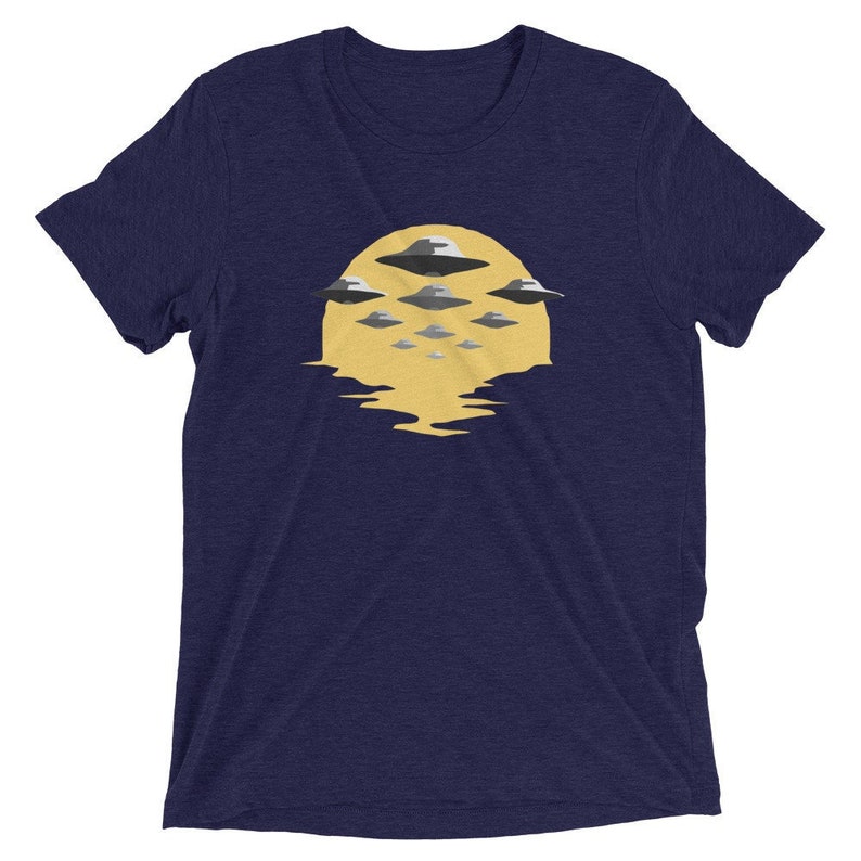 Puede incluir: Una camiseta azul marino con un gr&aacute;fico de un sol amarillo con varios OVNIs grises volando sobre &eacute;l.