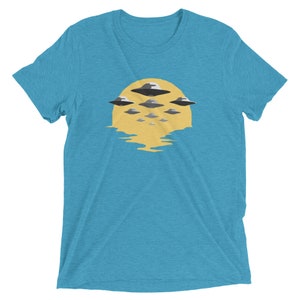 Puede incluir: Una camiseta azul turquesa con un gr&aacute;fico de un sol amarillo con m&uacute;ltiples OVNIs grises volando sobre &eacute;l.