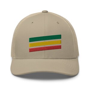 Puede incluir: Una gorra de camionero beige con un dise&ntilde;o de rayas verdes, amarillas y rojas bordado en la parte delantera.
