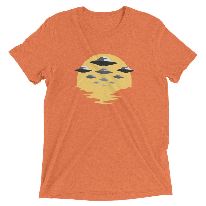 Puede incluir: Camiseta naranja con un gr&aacute;fico de un sol amarillo y m&uacute;ltiples platillos voladores en formaci&oacute;n.