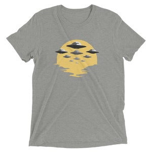 Puede incluir: Una camiseta gris jaspeada con un gr&aacute;fico de un sol amarillo y varios ovnis grises volando sobre &eacute;l.