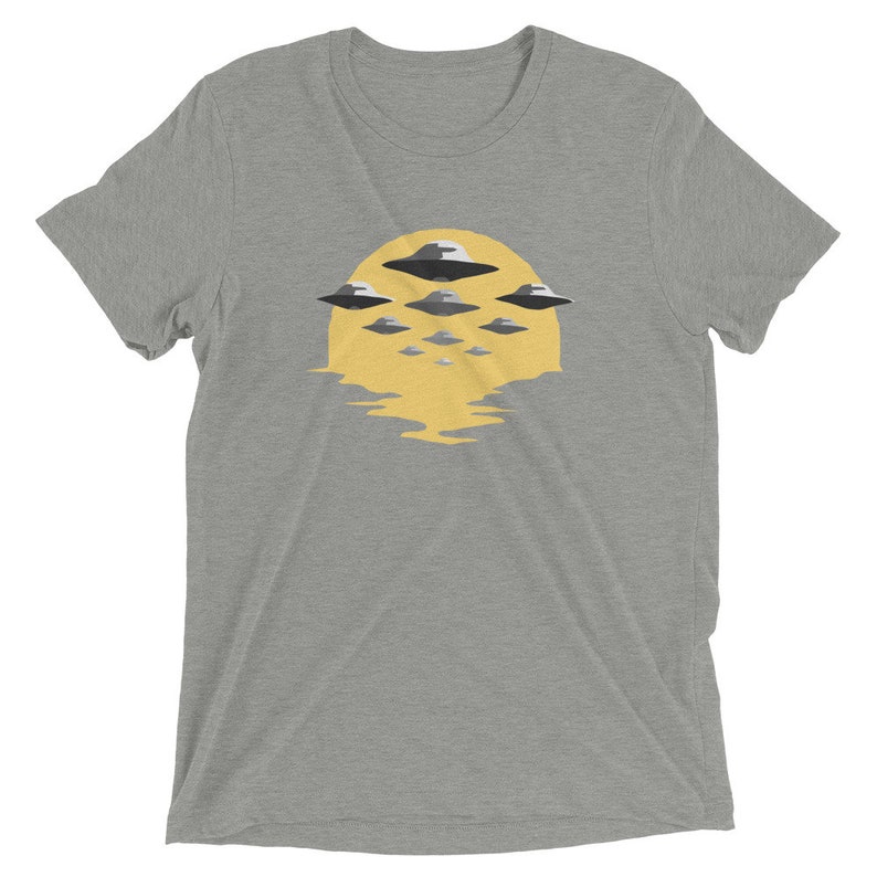 Puede incluir: Una camiseta gris jaspeada con un gr&aacute;fico de un sol amarillo y varios ovnis grises volando sobre &eacute;l.