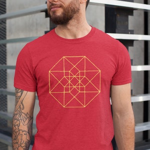 Może przedstawiać: Czerwony T-shirt z geometrycznym wzorem w kolorze żółtym. Wzór to duży ośmiokąt z mniejszym ośmiokątem wewnątrz. Wzór składa się z linii tworzących wzór siatki.