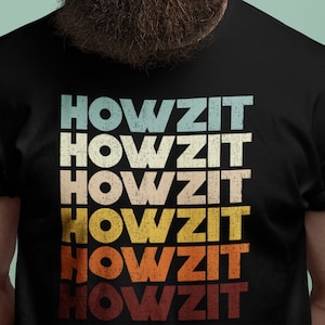 以下が含まれることがあります： レトロなフォントで「HOWZIT」の文字が5回重ねられた黒いTシャツ。テキストは青、黄、オレンジ、赤の色合いです。画像に写っている人物はサングラスをかけており、長いひげを生やしています。