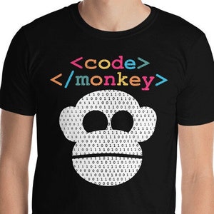 Może przedstawiać: Czarny T-shirt z białą małpią twarzą wykonaną z kodu binarnego. Tekst "<code>/monkey>" jest nadrukowany na koszulce w kolorach tęczy.