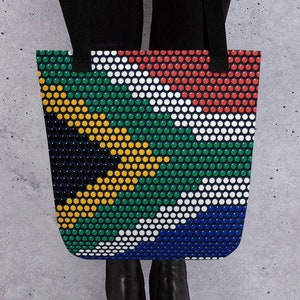 May include: A black tote bag with a South African flag design. The flag is made up of small circles in the colors of the South African flag: green, yellow, black, white, and red.