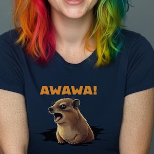 以下が含まれることがあります： 虹色の髪をした女性が、漫画の動物のグラフィックと「AWAWA！」という文字がプリントされたネイビーブルーのTシャツを着ています。