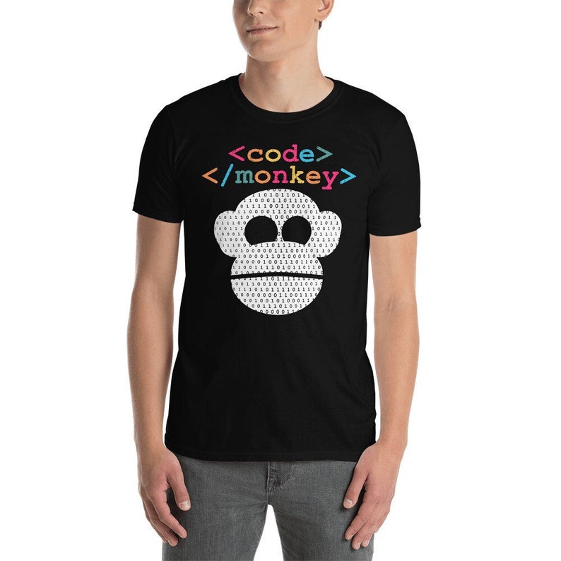 Może przedstawiać: Czarny T-shirt z białą małpią twarzą wykonaną z kodu binarnego. Tekst "<code>/monkey>" jest nadrukowany na koszulce w kolorach tęczy.