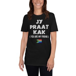 May include: Black t-shirt with white text that reads "Jy Praat Kak (You Are My Friend)" and a South African flag.