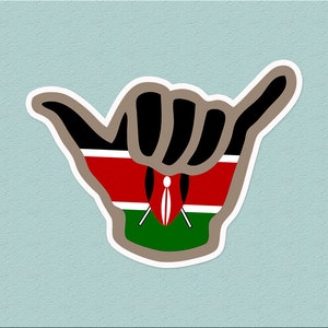Puede incluir: Un gesto de mano en forma de shaka, con los colores de la bandera de Kenia. La mano es negra, con rayas rojas, blancas y verdes, y un pequeño escudo con una lanza en el centro.