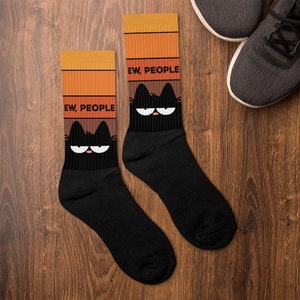 May include: A pair of black socks with a retro-style design featuring a black cat with the text "EW, PEOPLE" on each sock.