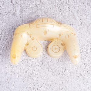 May include: A translucent yellow video game controller with a classic design. The controller features buttons, analog sticks, and a directional pad. The controller is made of a clear plastic material.