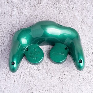 May include: A metallic emerald green video game controller with a distinctive shape. The controller has two circular buttons on the bottom and a Nintendo logo. The controller is designed for gaming.