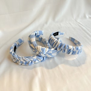 May include: Three blue and white gingham headbands with a knotted design. The headbands are made of a soft, stretchy fabric.