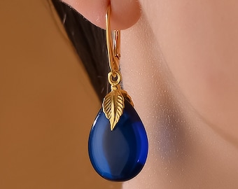 May include: Gold teardrop earrings with a blue gemstone and a small gold leaf detail.