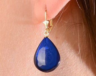 May include: Gold dangle earrings with a teardrop shaped blue gemstone.