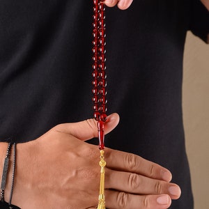 May include: A red amber prayer beads with a gold tassel. The beads are strung on a cord and the tassel is attached to the end of the cord.