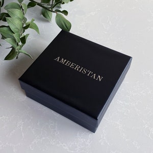 May include: A black square box with the word "AMBERISTAN" printed in gold lettering.