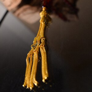 May include: A gold tassel with multiple strands hangs from a red beaded necklace. The tassel is made of intricate gold chain links.