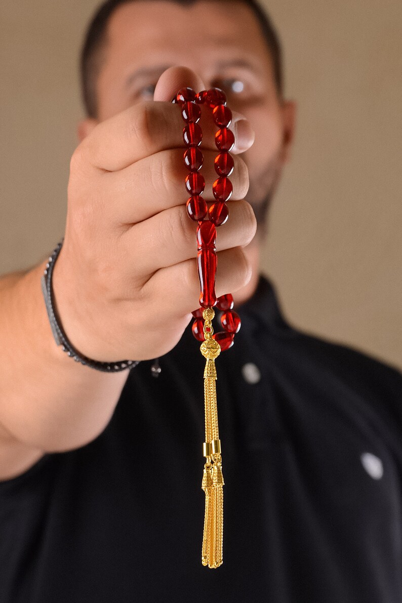 May include: A red prayer bead necklace with a gold tassel. The beads are strung on a cord and the tassel is attached to the end of the cord.