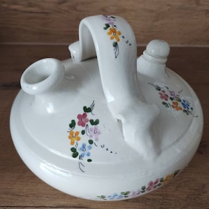 May include: White ceramic pitcher with a floral design in shades of pink, yellow, blue, and green. The pitcher has a handle and a spout.