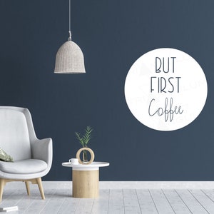 Pode incluir: Adesivo de parede circular branco com o texto "But first, coffee" em letras pretas em uma parede azul escura.