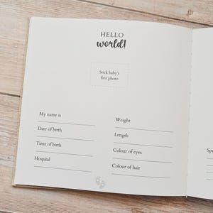 May include: Open baby memory book with the words "HELLO world!" in a handwritten style. The book has prompts to record baby's name, birth date, time, weight, length, eye and hair color, and hospital.