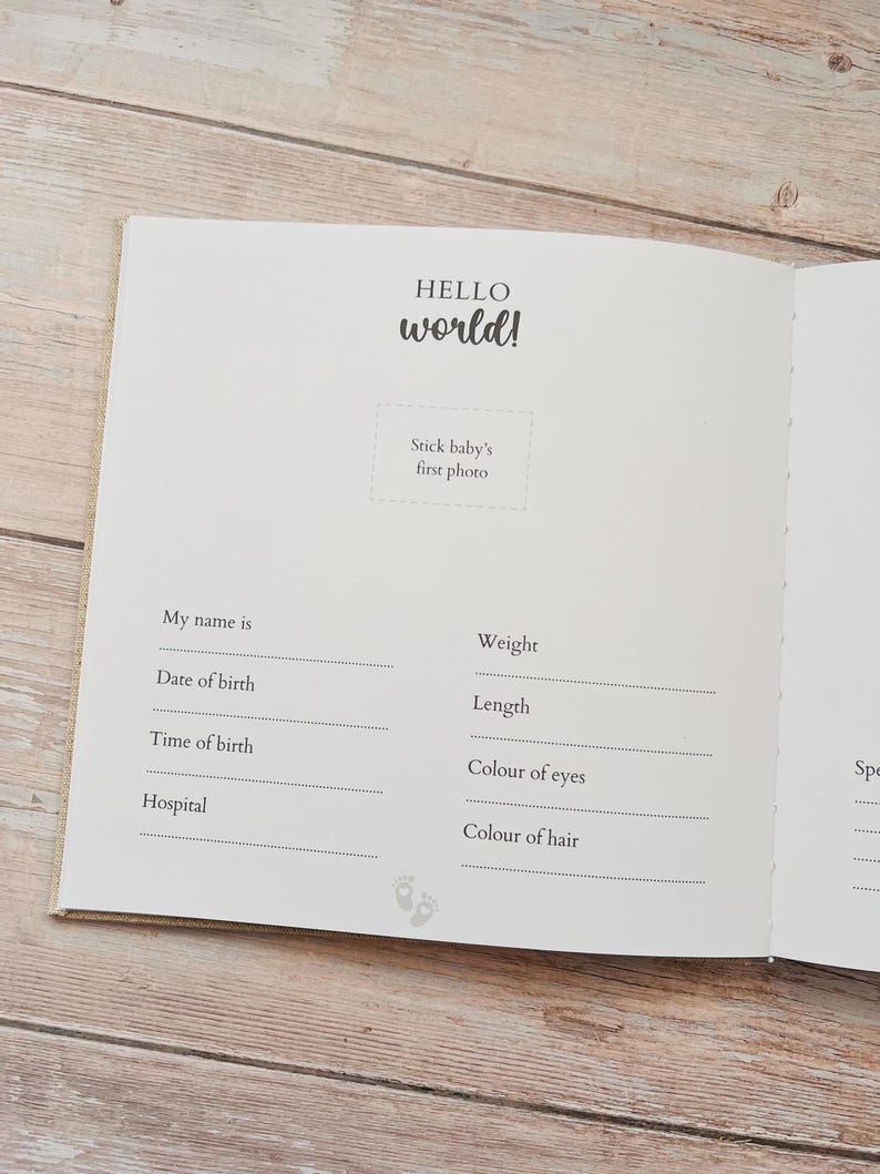 May include: Open baby memory book with the words "HELLO world!" in a handwritten style. The book has prompts to record baby's name, birth date, time, weight, length, eye and hair color, and hospital.